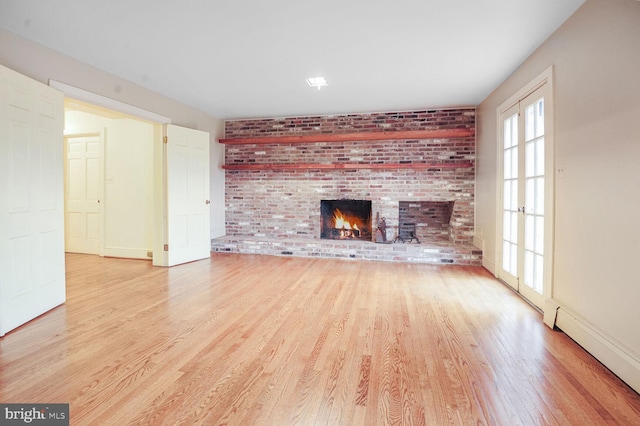 unfurnished living room featuring a baseboard heating unit, a brick fireplace, light wood-style flooring, and baseboards