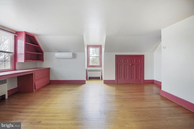 bonus room with baseboards, a wall mounted AC, built in study area, radiator, and light wood finished floors