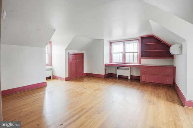 bonus room with light wood-style floors, radiator, built in study area, and an AC wall unit