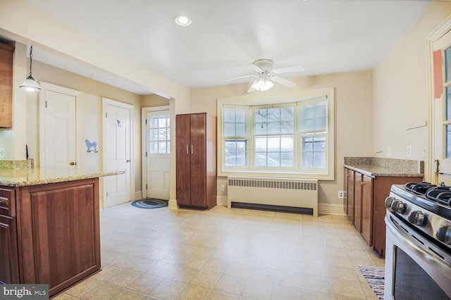 kitchen with stainless steel gas stove, baseboards, radiator, light stone countertops, and recessed lighting