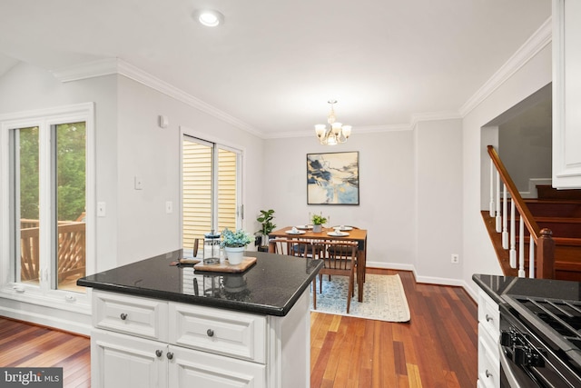 kitchen with range with gas stovetop, crown molding, wood-type flooring, white cabinets, and a chandelier