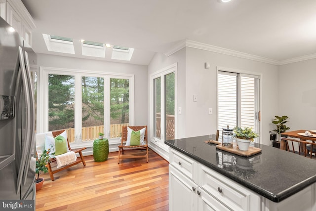 kitchen with a skylight, white cabinets, stainless steel fridge with ice dispenser, crown molding, and light wood-style floors