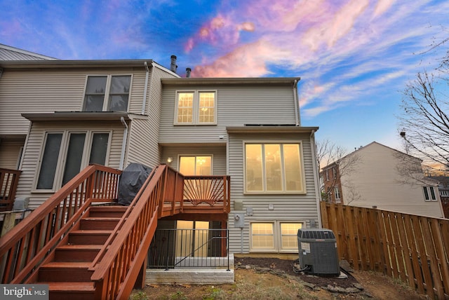 back of property at dusk with stairs, a deck, cooling unit, and fence