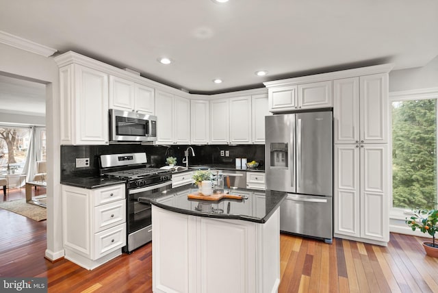 kitchen with stainless steel appliances, hardwood / wood-style floors, backsplash, and white cabinets