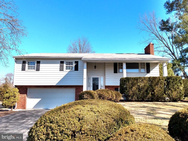 split foyer home featuring a garage, brick siding, a chimney, and aphalt driveway