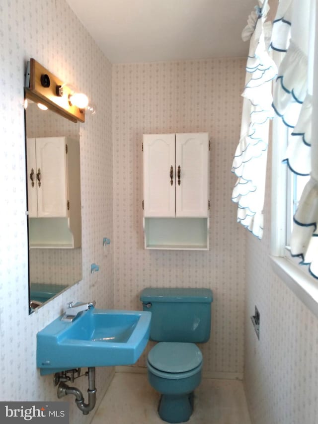 bathroom featuring toilet, wallpapered walls, a sink, and tile patterned floors