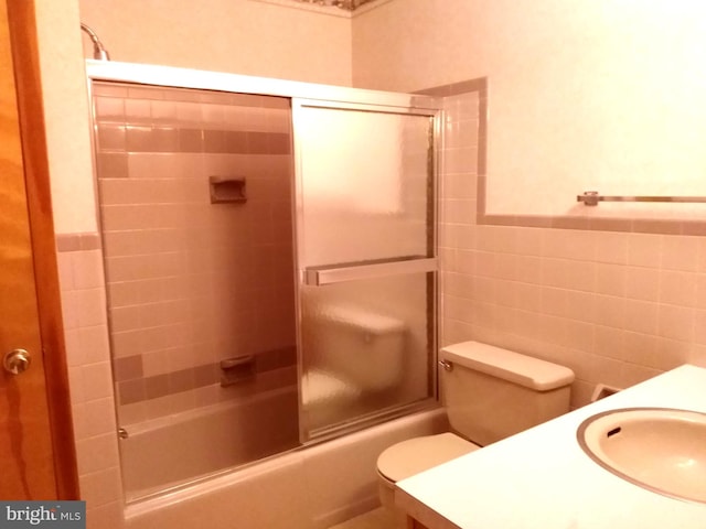 bathroom with a wainscoted wall, tile walls, toilet, combined bath / shower with glass door, and vanity