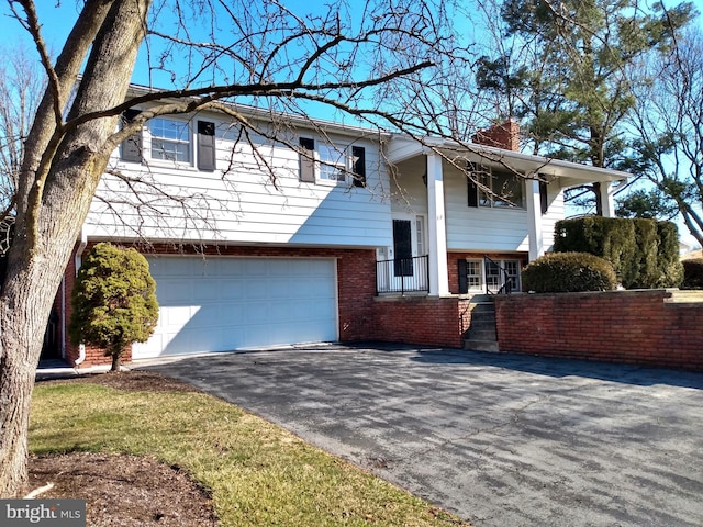 bi-level home with driveway, brick siding, a chimney, and an attached garage