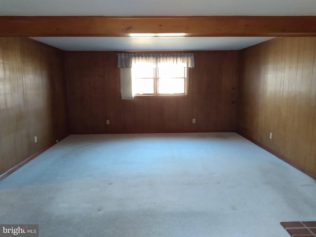 empty room with light colored carpet, beamed ceiling, and wooden walls