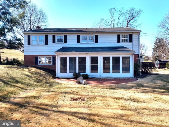 back of house featuring a sunroom, brick siding, and a lawn