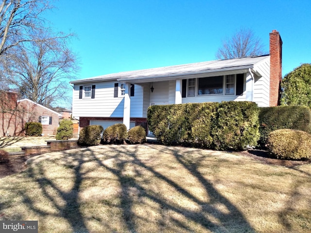 split foyer home featuring brick siding, a chimney, and a front yard