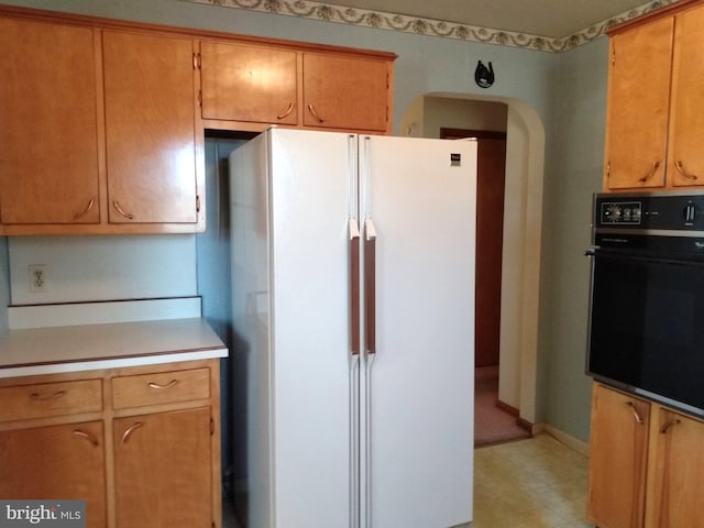 kitchen with baseboards, black oven, light countertops, freestanding refrigerator, and light floors