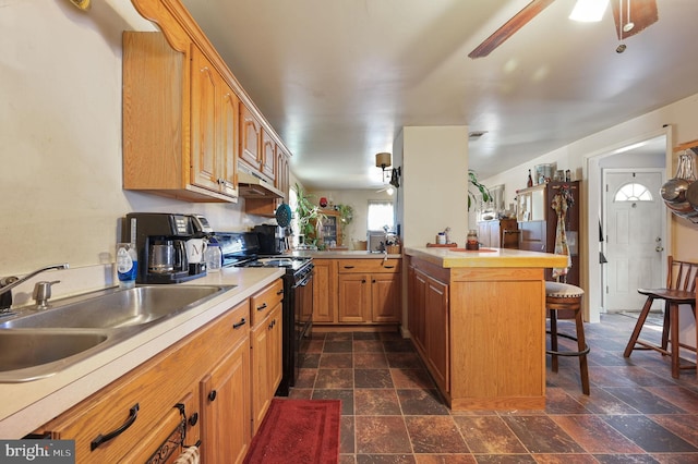 kitchen featuring ceiling fan, black range with gas cooktop, a breakfast bar area, and a peninsula