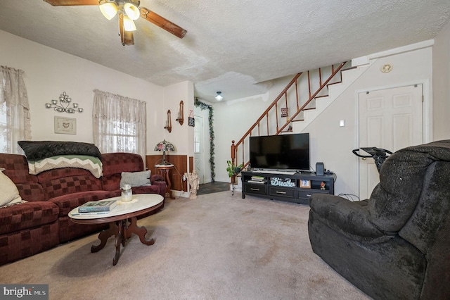 living area featuring a ceiling fan, carpet flooring, a textured ceiling, and stairs