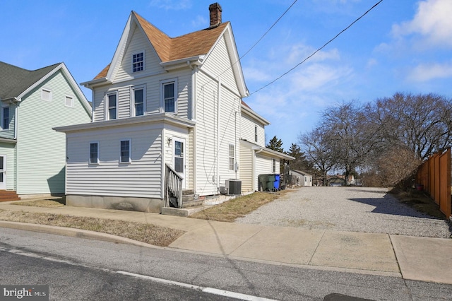 view of side of property with entry steps, driveway, a chimney, fence, and central AC