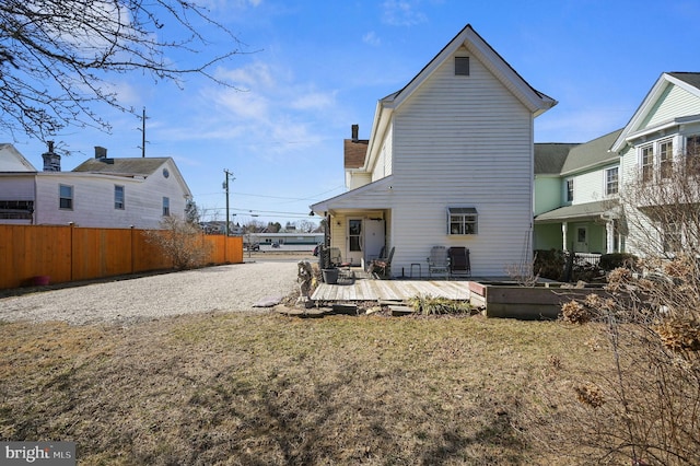 rear view of property with a deck, fence, a yard, a chimney, and gravel driveway