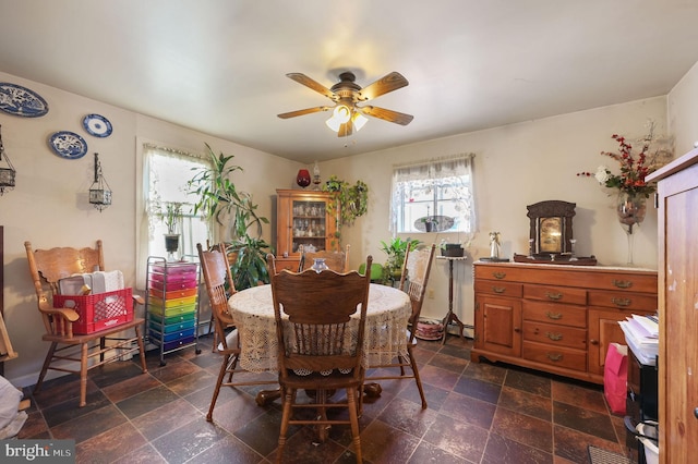 dining space with a ceiling fan, stone finish floor, a healthy amount of sunlight, and a baseboard heating unit