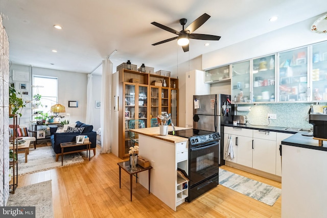 kitchen featuring black range with electric stovetop, decorative backsplash, freestanding refrigerator, and light wood-style floors