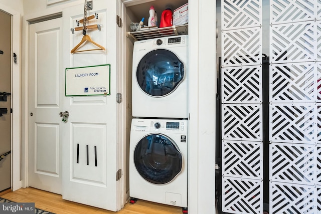 clothes washing area featuring stacked washer / dryer, laundry area, and light wood-style flooring