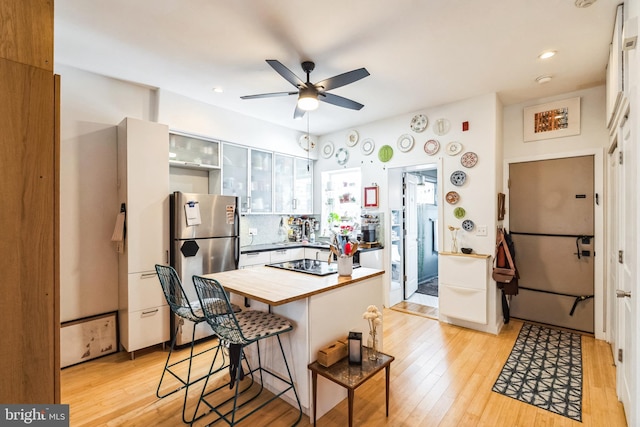 kitchen with a breakfast bar, wood counters, light wood-type flooring, backsplash, and freestanding refrigerator