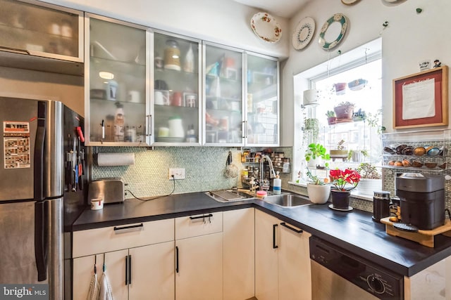 kitchen with dark countertops, glass insert cabinets, appliances with stainless steel finishes, a sink, and backsplash