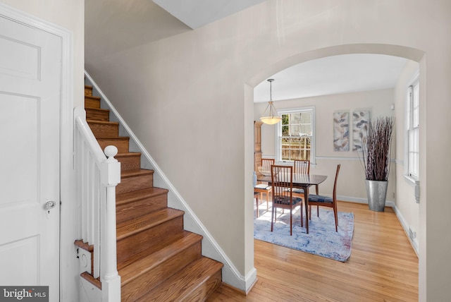 stairs featuring wood finished floors, arched walkways, and baseboards