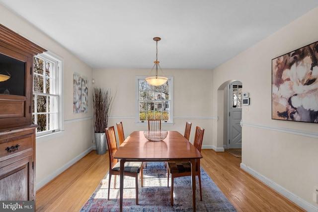 dining space with arched walkways, light wood-style flooring, and baseboards