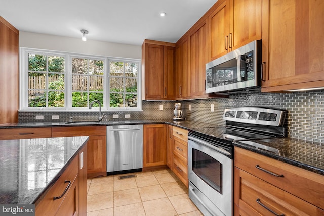 kitchen with brown cabinetry, backsplash, appliances with stainless steel finishes, and dark stone counters