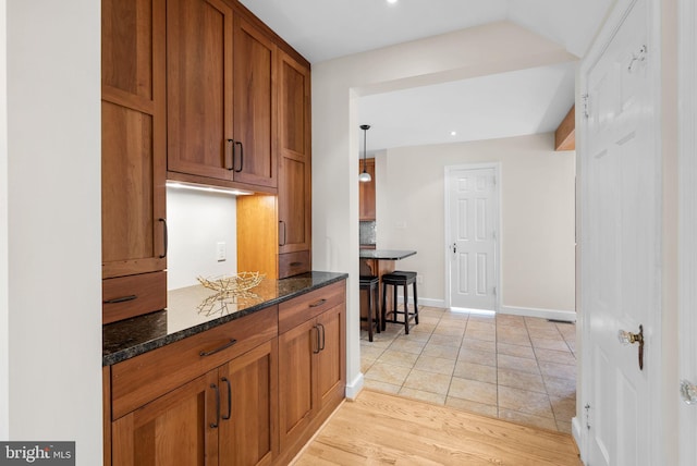 kitchen featuring brown cabinetry, dark stone countertops, light wood-style floors, and baseboards