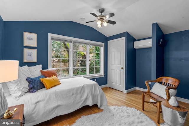 bedroom featuring lofted ceiling, wood finished floors, baseboards, and a wall mounted air conditioner