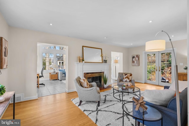 living room featuring visible vents, light wood finished floors, recessed lighting, french doors, and a glass covered fireplace