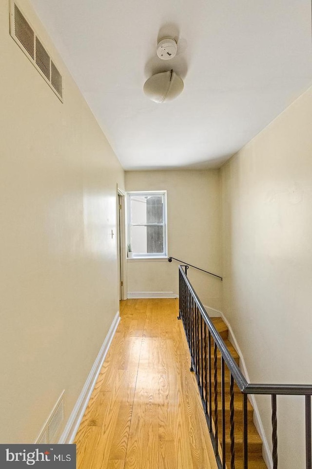 hallway with light wood-type flooring, visible vents, and baseboards