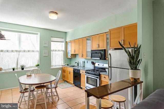 kitchen featuring light tile patterned floors, baseboards, glass insert cabinets, black appliances, and a sink