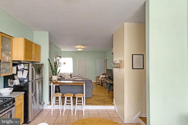 kitchen with light tile patterned floors, glass insert cabinets, appliances with stainless steel finishes, open floor plan, and baseboards