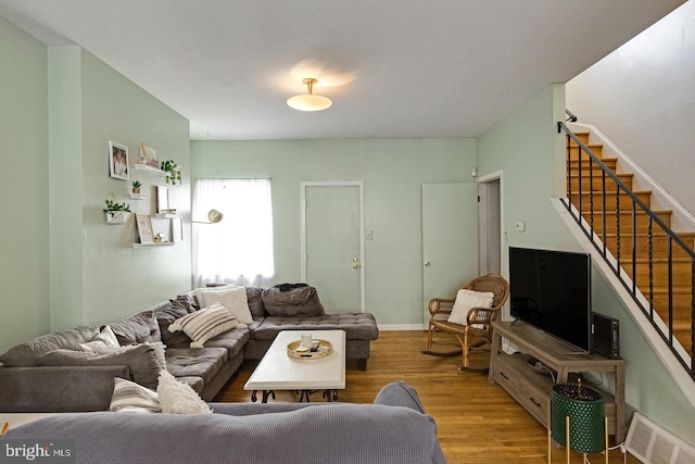 living area featuring baseboards, visible vents, stairway, and wood finished floors