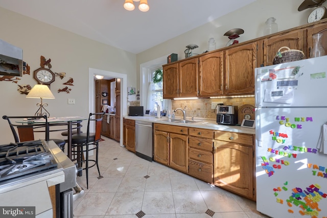 kitchen with a sink, stainless steel dishwasher, freestanding refrigerator, light countertops, and decorative backsplash