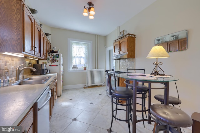 kitchen featuring a sink, gas stove, radiator, light tile patterned floors, and dishwashing machine