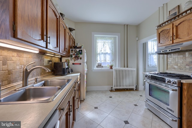 kitchen featuring baseboards, radiator heating unit, a sink, stainless steel range, and under cabinet range hood