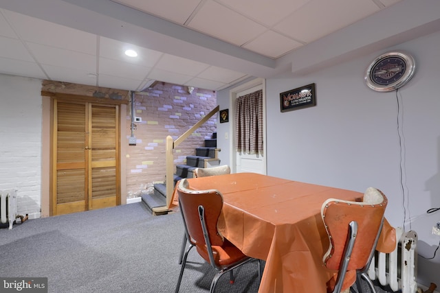 carpeted dining area featuring stairs, radiator, a paneled ceiling, and brick wall