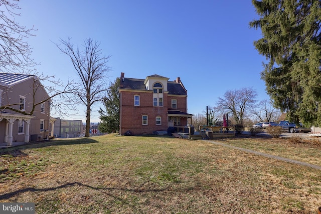 rear view of house featuring a lawn, brick siding, and a chimney