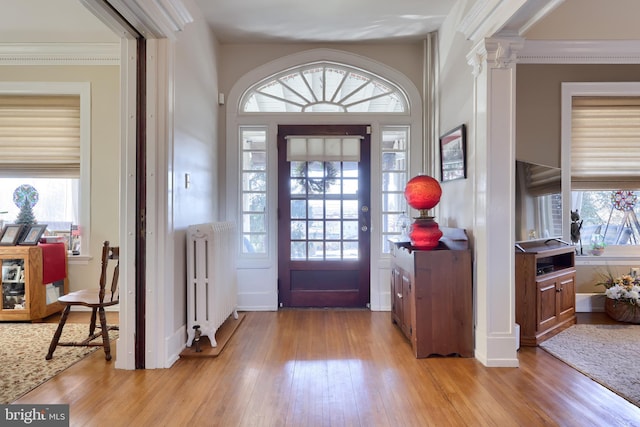 foyer with light wood finished floors, baseboards, radiator heating unit, ornamental molding, and ornate columns