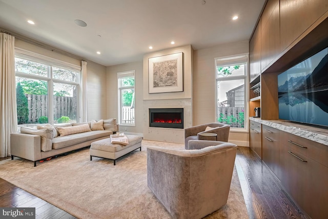 living area featuring recessed lighting, baseboards, a warm lit fireplace, and hardwood / wood-style floors