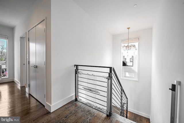 stairway featuring baseboards, an inviting chandelier, and wood finished floors