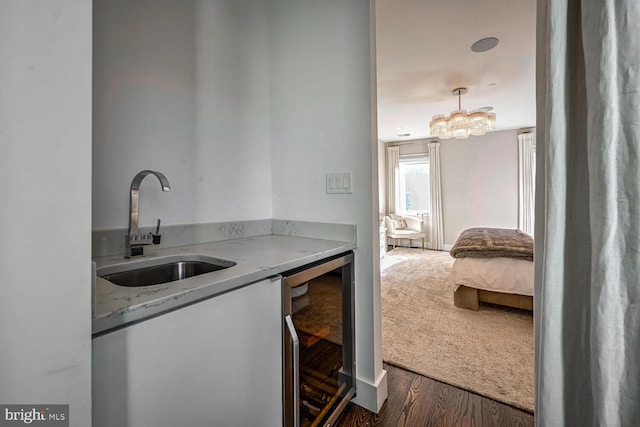 clothes washing area with beverage cooler, a sink, wood finished floors, carpet floors, and an inviting chandelier