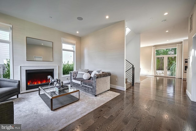 living room featuring dark wood finished floors, stairway, a warm lit fireplace, and a wealth of natural light