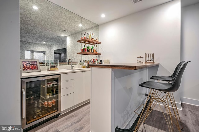 bar with beverage cooler, bar, light wood-type flooring, and a sink