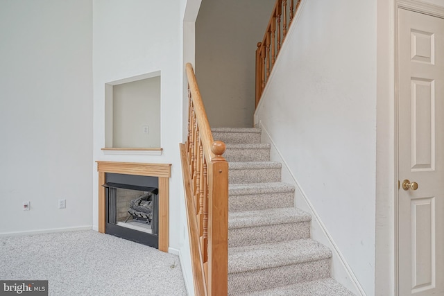 staircase featuring baseboards, a fireplace, and carpet flooring