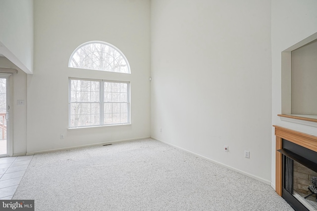 unfurnished living room featuring plenty of natural light, carpet flooring, a fireplace, and a towering ceiling