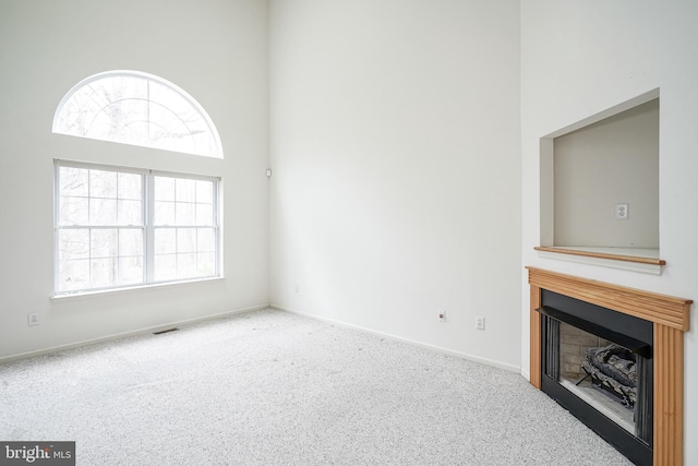 unfurnished living room featuring a fireplace, baseboards, carpet, and a towering ceiling