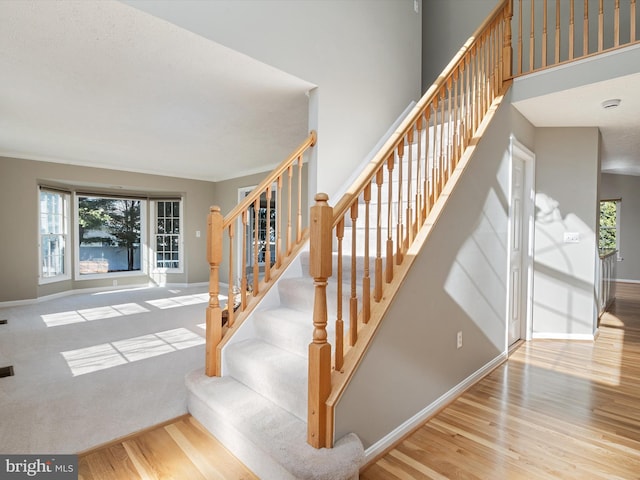 stairs with a towering ceiling, baseboards, and wood finished floors